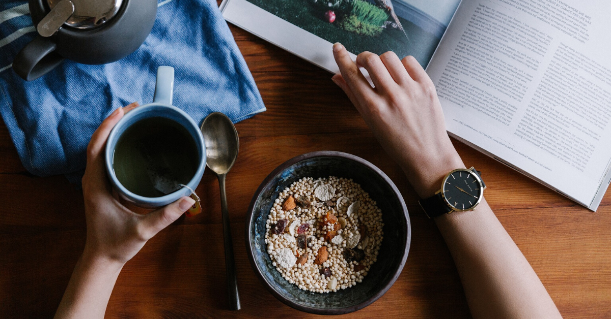 woman eating oatmeal for breakfast while she reads a book and sips tea